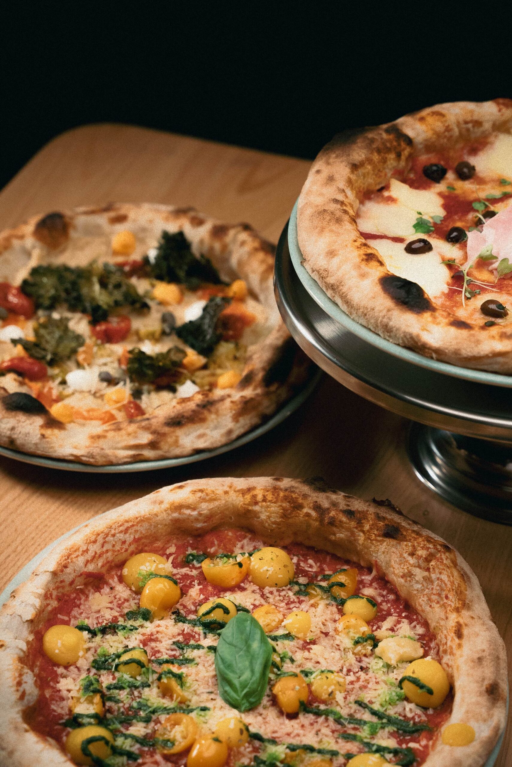 Tres pizzas dispuestas de manera decorativa sobre una mesa de madera de Sestogusto
